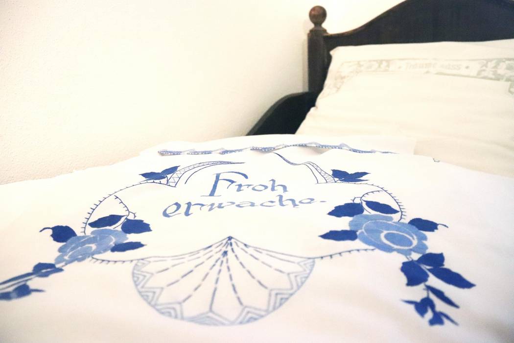 Eine weiße Bettdecke. Diese ist mit blauem Ornamenten und Schrift verziert.